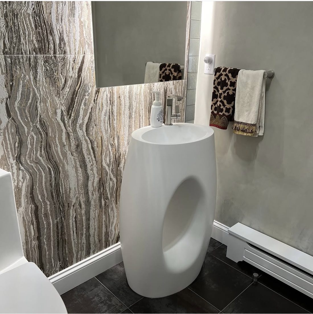 Minimalist bathroom with sculptural pedestal sink and marbled feature wall