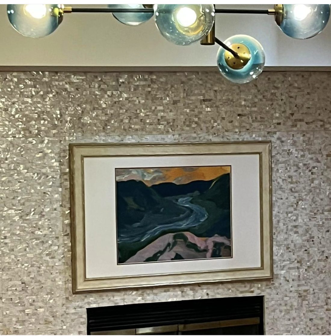 Cozy corner with shimmering mosaic tile fireplace wall, framed landscape art, and glass globe chandelier