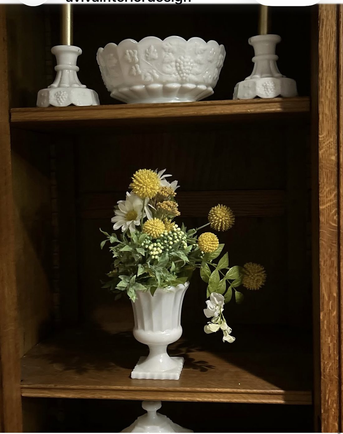 Curated milk glass collection styled on wooden shelves with floral arrangement